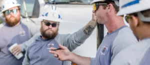 Utility crew members in hard hats communicating beside a work vehicle